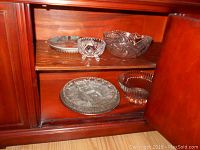 Glass trays and bowls displayed in a wooden cabinet shelf showing a mix of sizes and shapes.