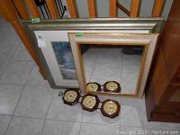 Set of framed mirror, framed picture, and four wooden barometers on tile floor near stairs