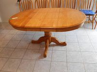 Wood kitchen table with straight edges and pedestal base, shown with leaves inserted, viewed from side angle.