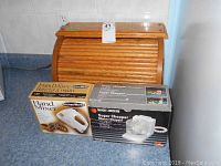 Wood bread box, Black & Decker Super Chopper in original box, KitchenWorks Hand Mixer in original box arranged on kitchen counter.