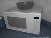 White Panasonic NN SG636 microwave on kitchen counter with clear plastic food cover on top.