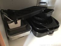 Image of various roasting pans and an electric griddle stacked in a cabinet, showing large, medium, and small black speckled roasters, along with griddle and other pans.