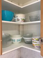 Two open corner shelves showing blue plastic bowl, Royal Worcester floral bowl, clear ribbed glass bowl, Pyrex mixing bowls with turquoise pattern, and a stack of clear glass fruit nappies with scalloped edges.