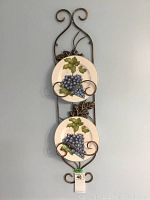 Vertical view of two decorative plates held in a metal stand with scroll design and metal leaves.