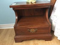 Front view of Kroehler wood nightstand with one drawer and decorative brass handle.