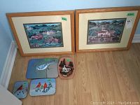 Wide shot showing the two framed Charles Wysocki prints on the floor next to four smaller painted items including enamel plates and a clay piece with keychain.
