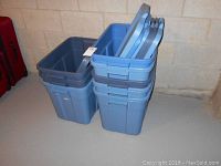 Stack of blue Rubbermaid storage bins with gray lids placed on top, showing sturdy plastic material and design.