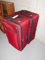 Two red Travel Select 27 inch suitcases stacked together showing side and top handles, fabric material, and zippered compartments.