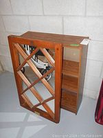 Shows angled view of wood framed mirror with criss-cross design and pressed board bookcase with shelves.