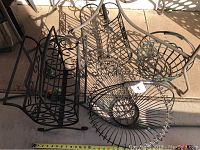 Photo showing four metal baskets placed on the ground with sunlight casting shadows. Includes a black rectangular basket with scrollwork, a large round basket with scalloped edges, and two smaller round baskets.