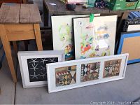 Photo of four framed art prints including three vertically standing colorful fish prints and one long horizontal Southwest geometric print, along with a framed star fish print leaning separately.