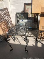 Photo of one metal outdoor table with curved legs and metal slatted top taken outside showing wear and other items around it.