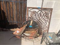 Photo showing three metal decorative items: a round mirror, a metal ornamental grate, and two metal boat sculptures on concrete floor outside.