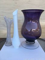 Three vases in one photo: from left to right, clear opalized bud vase, white milk glass bud vase, and large amythus purple vase.
