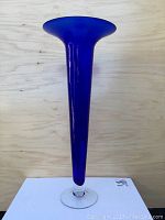 Tall cobalt blue glass trumpet vase with a clear glass base on a wooden background, showing whole vase.