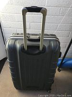 View of gray Samsonite rolling suitcase showing extended telescoping handle and textured hard shell.