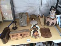 Photo shows a table with carved wooden items, Native American paintings, decorative pottery, and a metal candle holder.