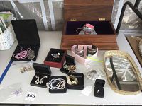 Full lot including opened wooden jewelry box with purple velvet lining, assorted costume jewelry in black and red jewelry boxes, hanging doll's head figurine, mirrored tray, and loose jewelry pieces on tabletop.
