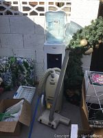 Full view of the Chicago water cooler with water bottle and Electrolux canister vacuum cleaner with hose and power head attachment, surrounding items and outdoor setting.