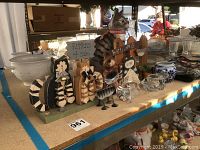 Cat decorations displayed on a table, including wooden cat figures with a sign, glass and metal cats, ceramic jar, and table runner.
