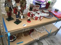 Photo showing four wooden nutcracker figures including three large soldiers and one smaller snowman figure beside various Christmas mugs and glass plates.
