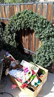Large green artificial Christmas wreath hanging on wooden fence with three boxes of Christmas decor underneath