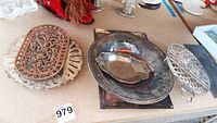 Photo showing three silver-plated trays of various shapes and sizes beside three decorative trivets with ornamental cast and wooden inlay designs.