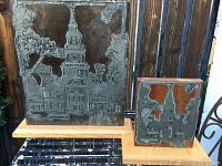 Front view of both antique etched printing plates mounted on wooden boards, showing detailed architectural designs with clock tower and buildings
