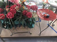 Woven basket with dense red faux flowers and greenery, metal support frame visible