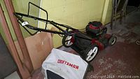 Side view of red Craftsman lawn mower with attached white collection bag and black handle.