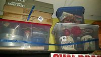 Plastic bins containing various kitchen and home decor items, stacked and secured with blue straps.