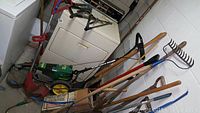 Photo showing yard tools including rakes, shovels, six outlet power stake, and green wheeled Weed Eater trimmer.