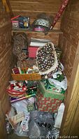 Full view of lot showing stacked Christmas tins, gift boxes, wrapping paper, bags, and various decorations in a wooden storage space.