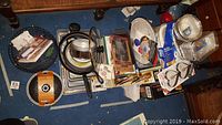 Overall view showing assortment of pans, waffle maker, foil containers, and kitchen utensils on floor under table.