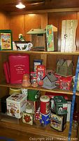 Shelf with various tins, red boxes, moose cups, decorative birdhouses, including a metal lidded bread box and silver plated jar