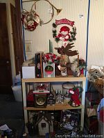 Full view of plastic shelving unit loaded with Christmas decorations including miniature village houses, snow globes, figurines, and wall hangings above the shelf