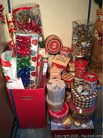 Photo of large red container filled with rolled Christmas gift wrap, alongside assorted decorative Christmas gift boxes and tins stacked nearby.