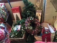 Photo showing two artificial Christmas trees, a wreath with red ribbon, various small ornaments, and garland in boxes.