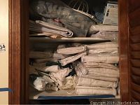 Shelf fully stocked with over 40 unopened packages of mostly white linen curtains folded and stacked.