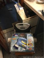 Photo of bathroom scale partially visible behind Black & Decker scrubber in original packaging on wooden stool.