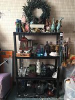 Full view of black plastic shelf unit holding assorted home decor items including animal figurines, glass bottles, wind chimes, candle holders, and wreath.