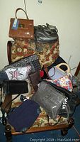 Overview of multiple purses and handbags arranged on a floral patterned armchair, showing various colors and styles with some tags visible
