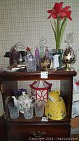 Full view of glassware, ceramic items, decorative candle holders, bottles, pitcher, plates, cookie jar, floral teapot, and artificial flowers arranged on wood shelving unit.