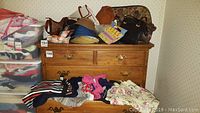 Photo shows hats, purses, and folded plus size women's clothing on and inside a wooden dresser.