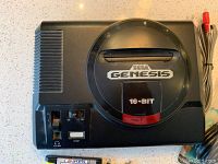 Top view of Sega Genesis console showing the 16-BIT logo, power and reset buttons, volume slider, and a game cartridge slot. The console is black with visible wear and marks.