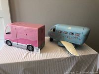 Side view of pink Barbie RV and blue vintage Barbie airplane showing airplane windows and RV closed side