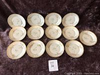 Overview of 13 round Limoges dessert plates arranged in rows, showing the floral pattern and gold gilt edges.