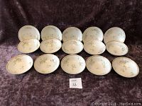 Set of 15 Limoges bowls with floral design and gold gilt rims, arranged in three rows on fabric background.