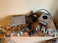 Sony PlayStation and Nintendo GameCube consoles with controllers and cables spread on table.