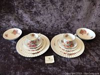 Two place settings of Royal Albert Centennial Rose bone china displayed with all items including dinner plates, salad plates, bread & butter plates, teacups, and saucers with a floral rose pattern.